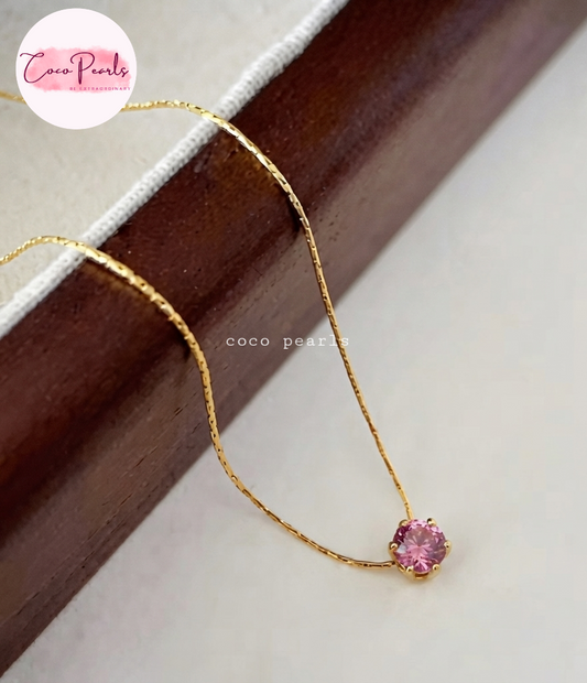 Coco pearls stainless Steel anti tarnish gold chain necklace with a small pink gemstone pendant, displayed on a dark wooden block