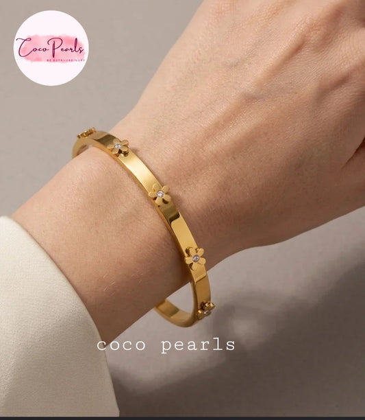 Coco pearls stainless Steel anti tarnish gold-plated bangle bracelet with small flower charms, worn on a person's wrist