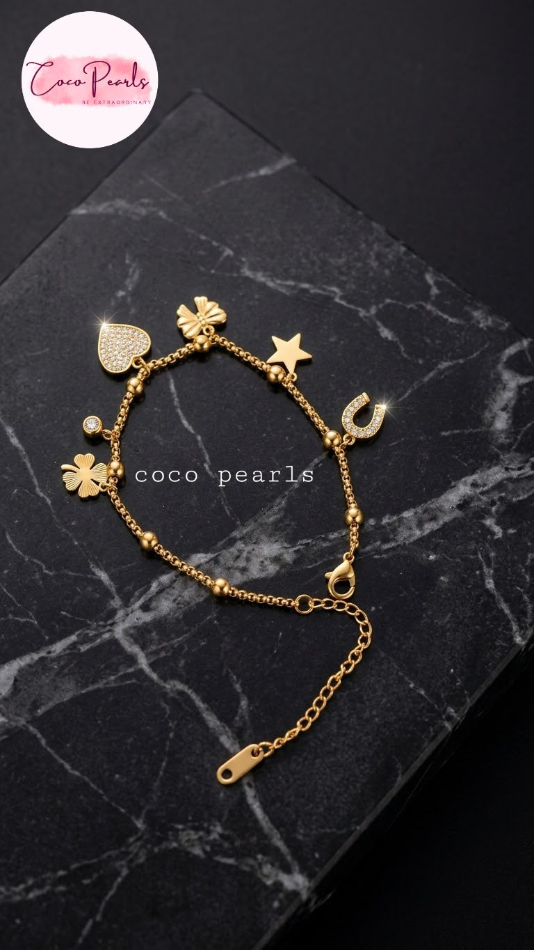 Coco pearls stainless Steel anti tarnish gold charm bracelet with multiple charms including a heart, clover, star, horseshoe, and flower, displayed on a black marble block.