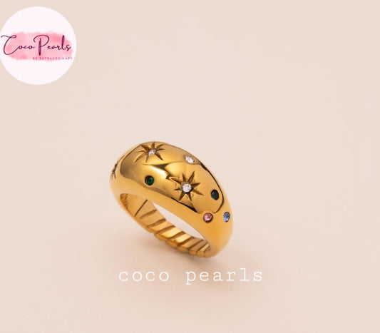 Coco pearls stainless Steel anti tarnish gold ring with a textured, ribbed band and a dome-shaped top decorated with star motifs and small colored gemstones, shown on a light beige background