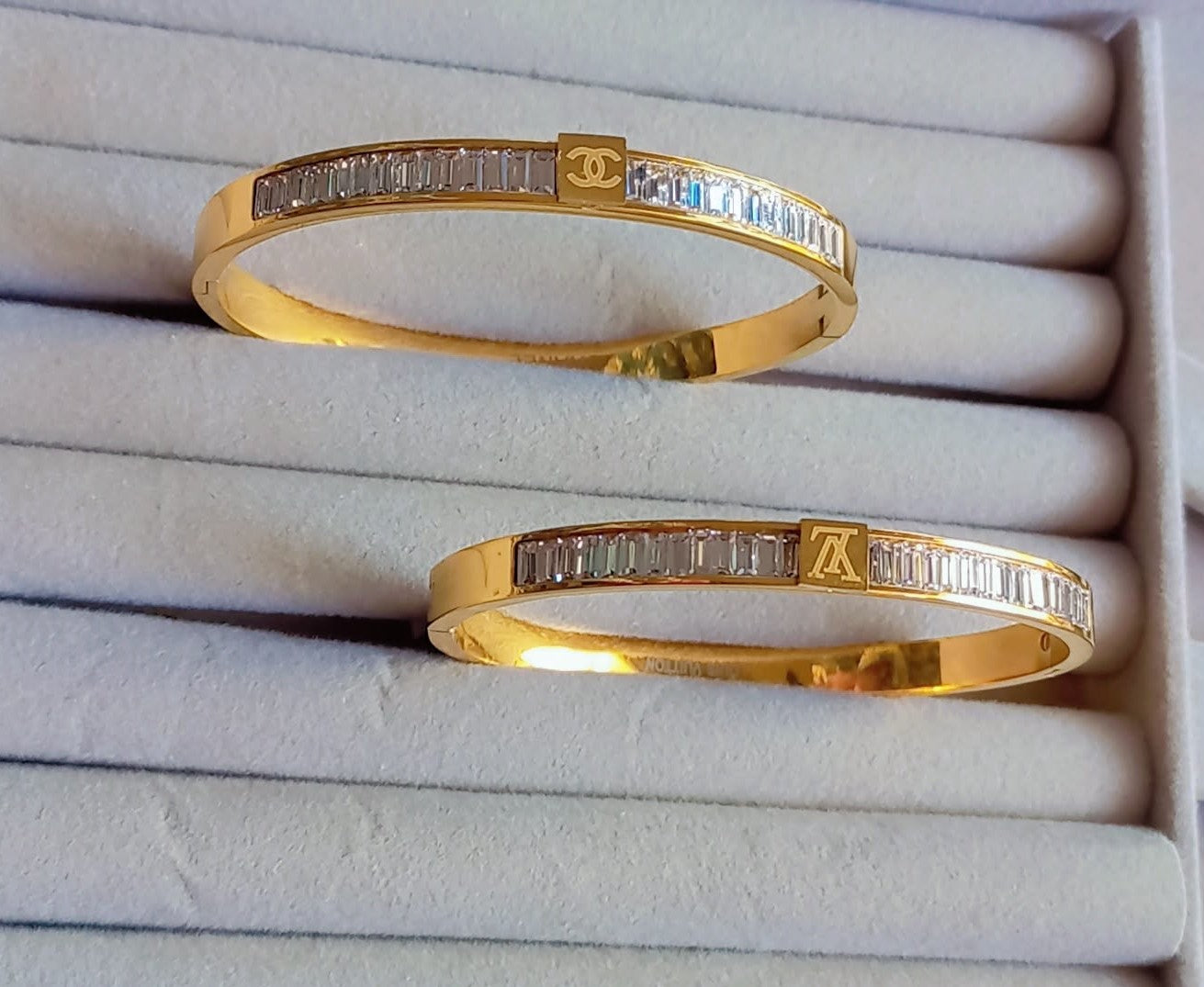 Coco Pearls Stainless Steel Anti Tarnish Two aura diamond line gold handcuff bangle bracelets with diamond accents on a white cushioned surface