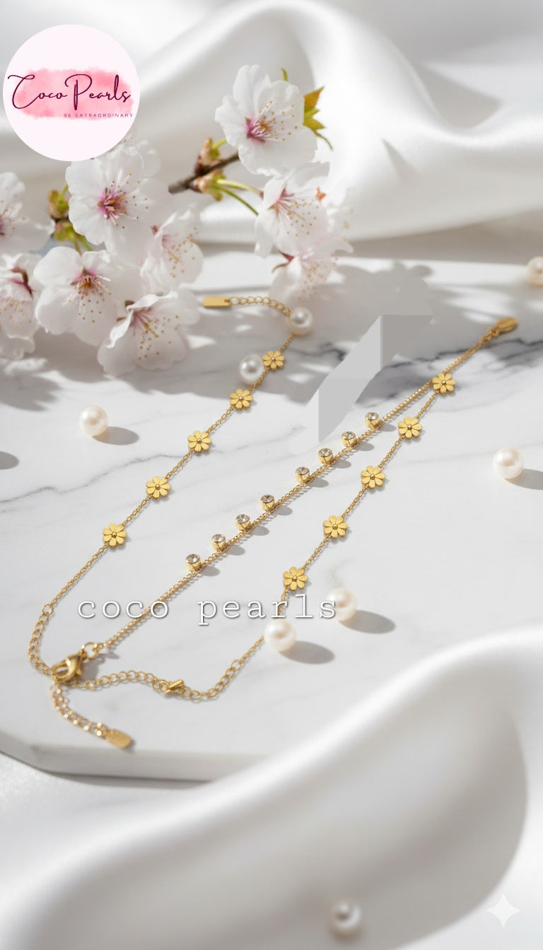 Coco Pearls Stainless steel anti tarnish Gold necklace with floral designs on a white fabric background with cherry blossoms.