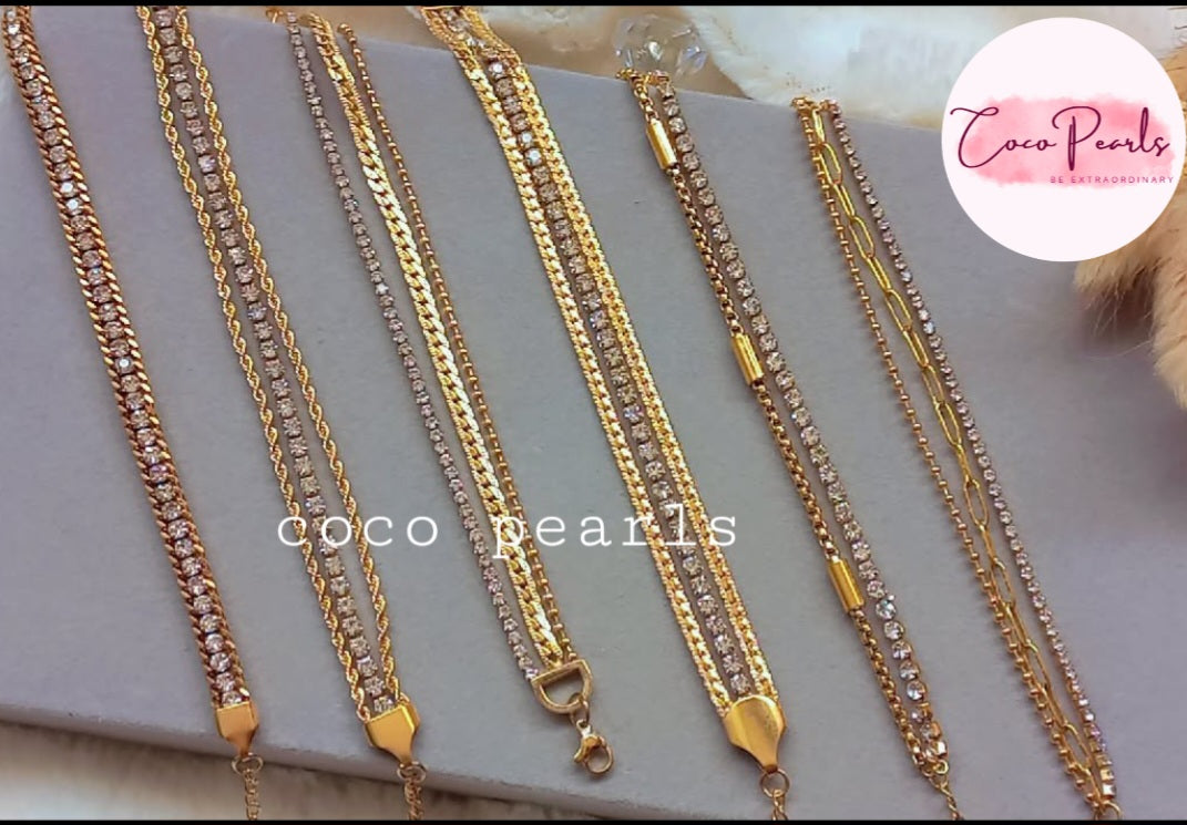 Coco Pearls Stainless Steel Anti tarnish Gold bracelets stack. Gold bracelets with rhinestones displayed on a gray surface