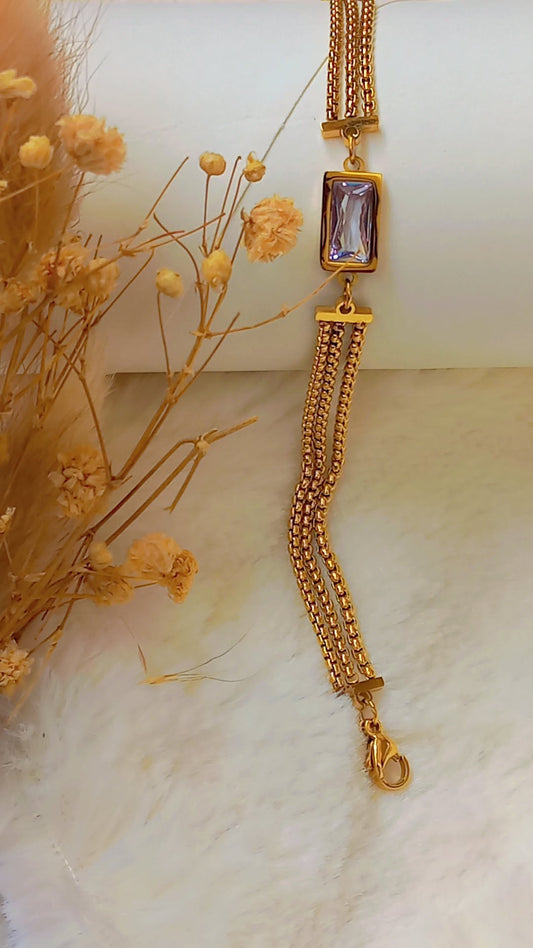 Coco Pearls Stainless Steel Anti Tarnish Gold crystal accent bracelet with a clear gemstone 3 layer chain on each side on a marble surface with dried flowers.