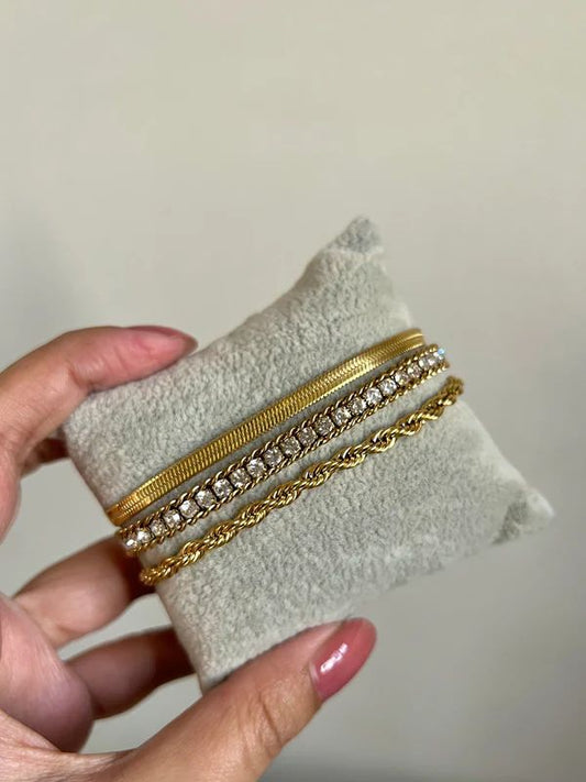 Coco Pearls Stainless Steel Anti Tarnish Three gold bracelets. one snake chain bracelet, one diamond accent bracelet and rope bracelet combo on a white cushion held by a hand