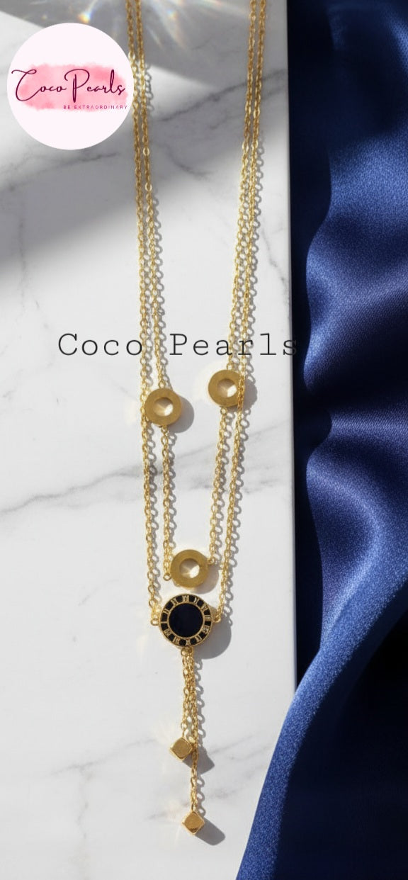 Coco Pearls Stainless Steel Anti Tarnish Gold chain cascade necklace with a black and gold circles and two hangings on a white and blue satin background