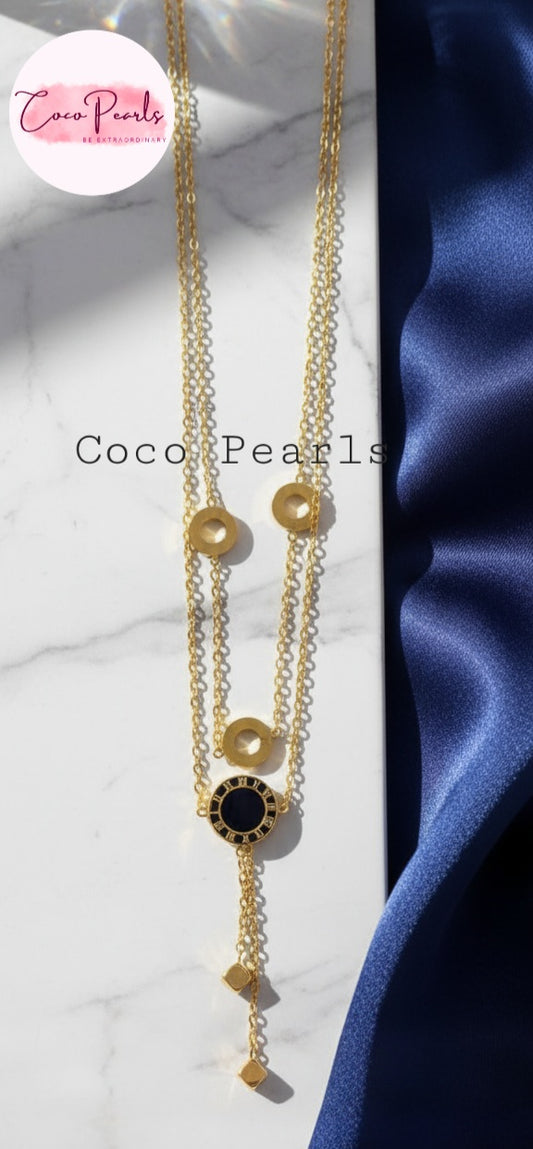 Coco Pearls Stainless Steel Anti Tarnish Gold chain cascade necklace with a black and gold circles and two hangings on a white and blue satin background