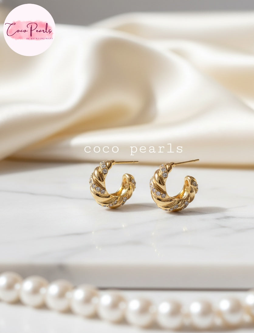 Coco Pearls Stainless Steel Golden whirl hoop croissant shaped earrings with rhinestones on a marble surface