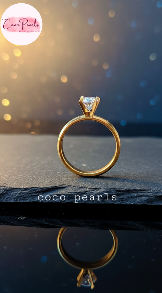 coco pearls stainless steel anti tarnish Gold luminous solitaire ring with a clear gemstone on a dark surface