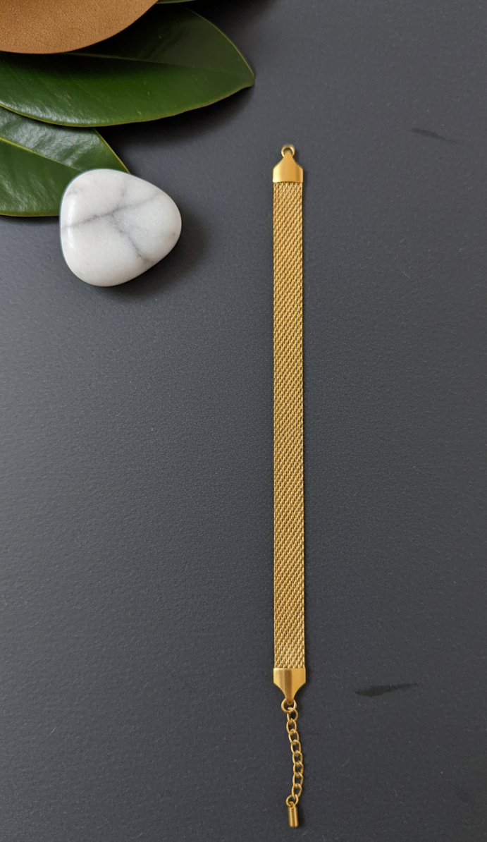 Coco Pearls Stainless Steel Anti tarnish Gold mesh bracelet on a dark surface with green leaves and a white stone.