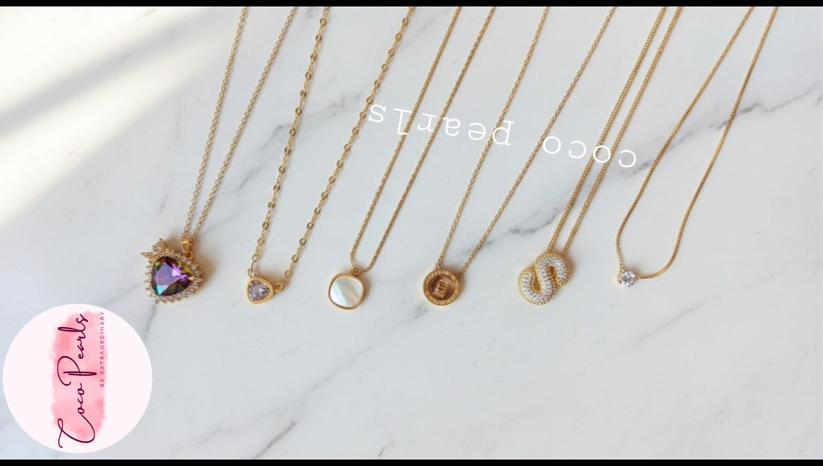 Coco Pearls Stainless Steel Anti Tarnish Gold necklaces with various pendants on a white marble surface