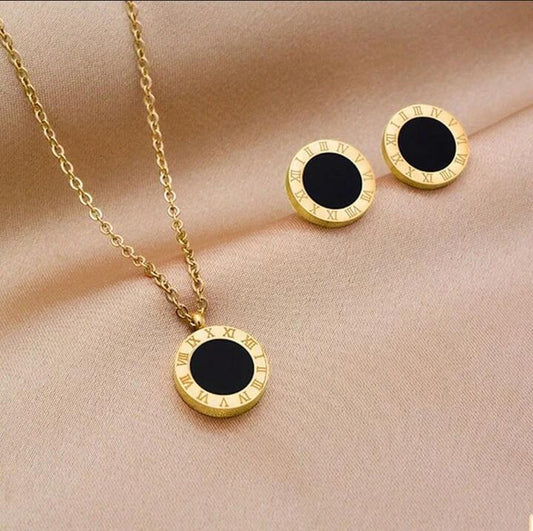 Coco Pearls Stainless Steel Anti Tarnish Gold roman accent set necklace and earrings with black stones on a beige fabric background