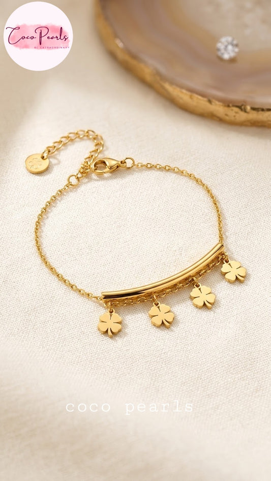 Coco pearls stainless Steel anti tarnish delicate gold chain bracelet with a curved bar and three dangling clover charms, displayed on a textured cream fabric
