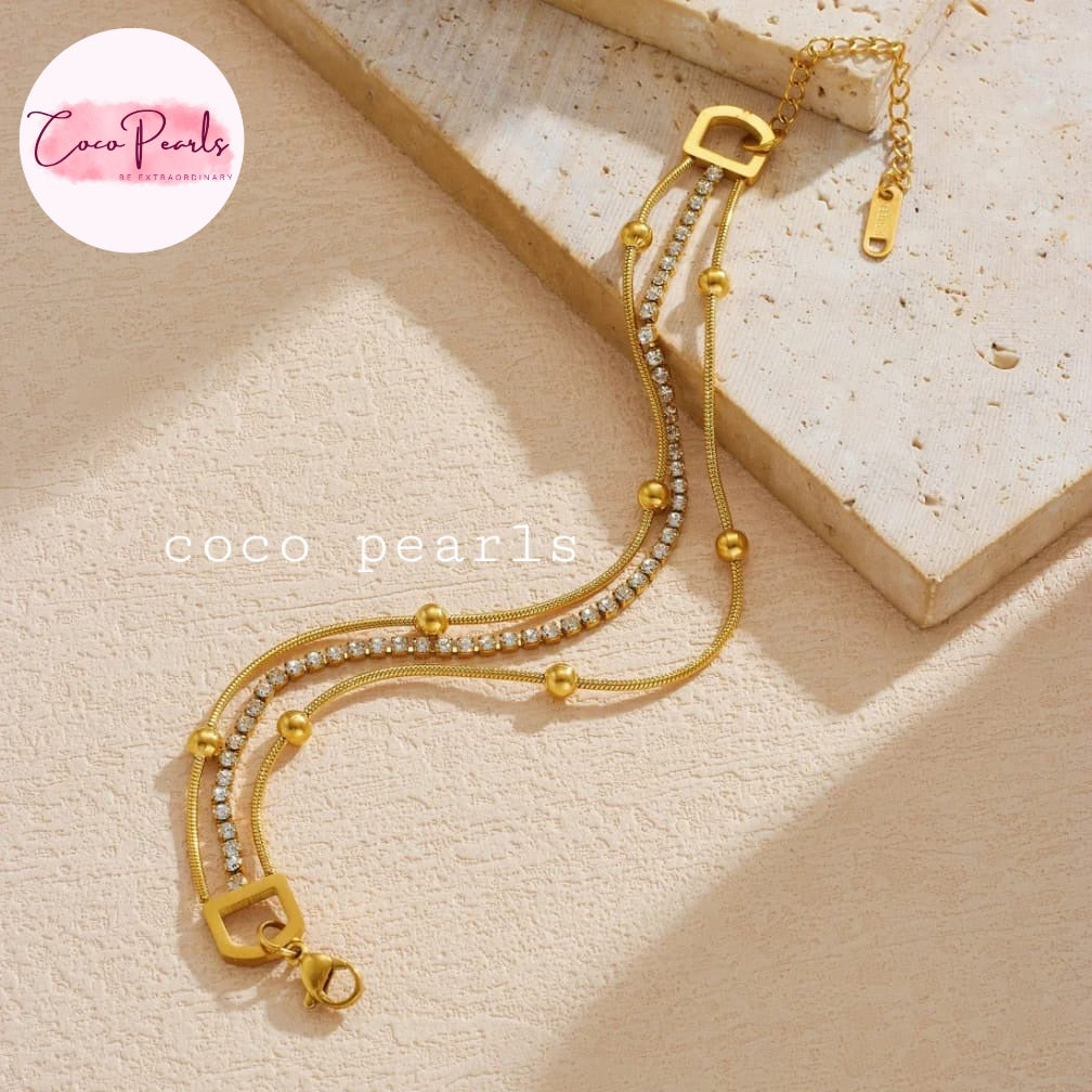 Coco pearls stainless Steel anti tarnish gold-toned multi-strand chain bracelet with small clear rhinestones and gold beads, displayed on a textured beige surface
