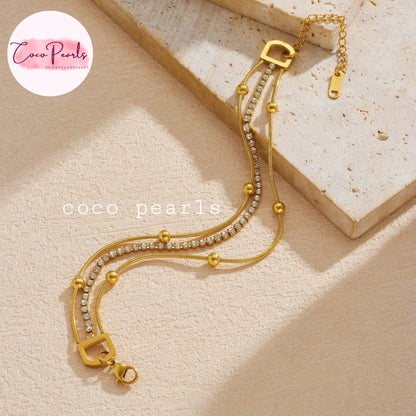 Coco pearls stainless Steel anti tarnish gold-toned multi-strand chain bracelet with small clear rhinestones and gold beads, displayed on a textured beige surface
