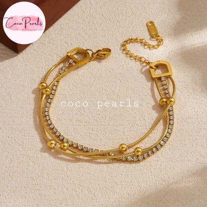 Coco pearls stainless Steel anti tarnish gold multi-strand bracelet with snake chain, clear crystal accents, and gold beads, displayed on a textured beige surface