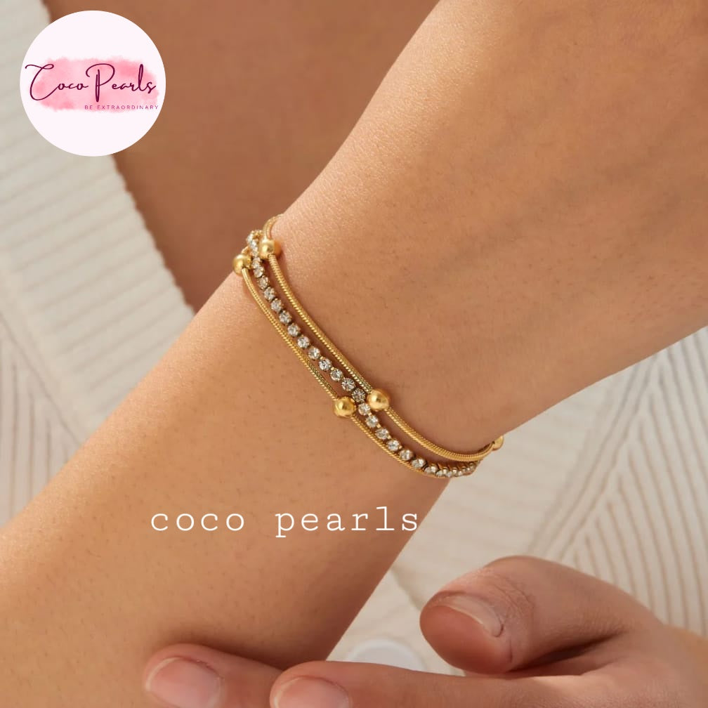 Coco pearls stainless Steel anti tarnish close-up of a person's wrist wearing a delicate gold double-strand bracelet with clear rhinestones and small gold bead accents.