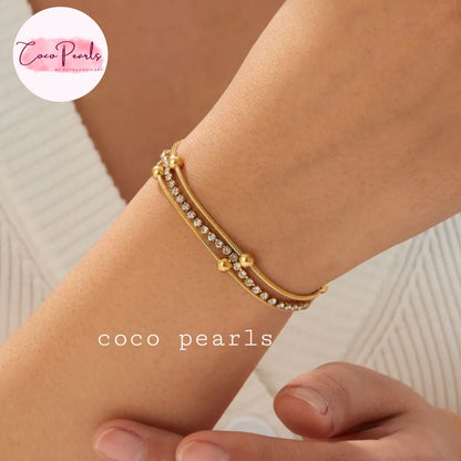 Coco pearls stainless Steel anti tarnish close-up of a person's wrist wearing a delicate gold double-strand bracelet with clear rhinestones and small gold bead accents.