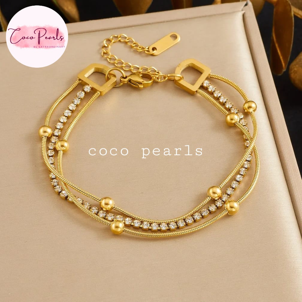 Coco pearls stainless Steel anti tarnish gold multi-strand bracelet with rhinestone accents and gold beads, displayed on a beige jewelry box.