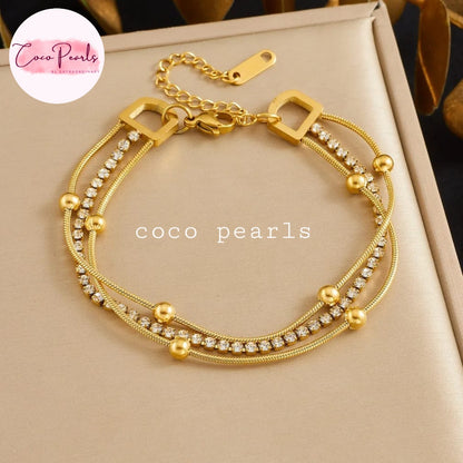 Coco pearls stainless Steel anti tarnish gold multi-strand bracelet with rhinestone accents and gold beads, displayed on a beige jewelry box.