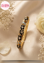 Coco pearls gold-plated bangle bracelet with black and white enamel floral detailing, displayed on a beige satin fabric with dried flowers