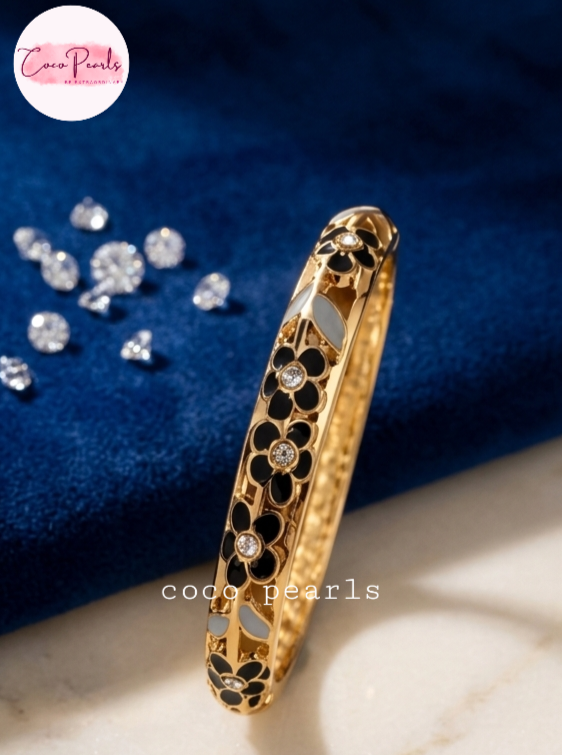 Coco pearls gold plated bangle bracelet with black and white enamel floral detailing and small clear rhinestones, displayed on a blue velvet surface