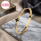 Coco pearls stainless Steel anti tarnish gold clover luxe diamond studded black clover charm in center handcuff displayed on marble surface 