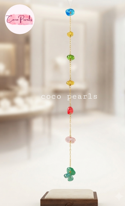 Coco pearls stainless Steel anti tarnish vertical gold-tone chain ornament featuring colorful polished stone beads in blue, yellow, green, amber, red, pink, and teal, hanging above a display stand. 