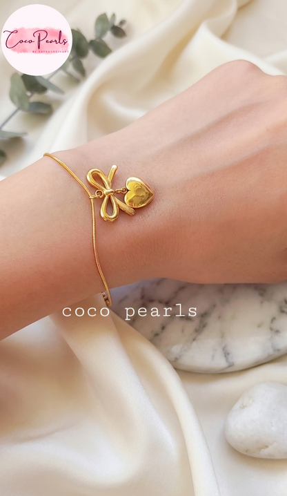 Stainless Steel anti tarnish Gold bracelet with a heart and bow design on a wrist, branded 'Coco Pearls', against a marble background.
