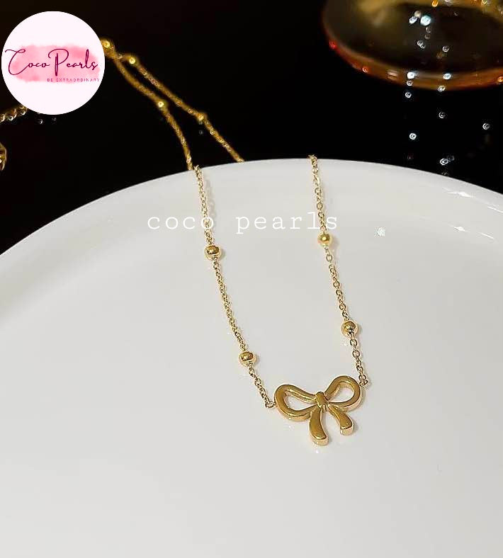 Coco pearls stainless Steel anti tarnish gold necklace with a bow-shaped pendant and small bead accents, displayed on a white plate.