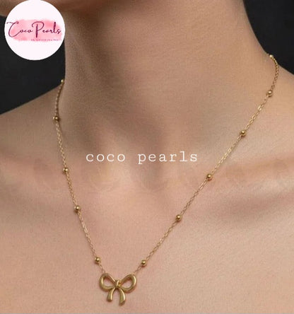 Coco pearls stainless Steel anti tarnish gold necklace with a small bow pendant and small bead accents, shown worn on a model's neck.