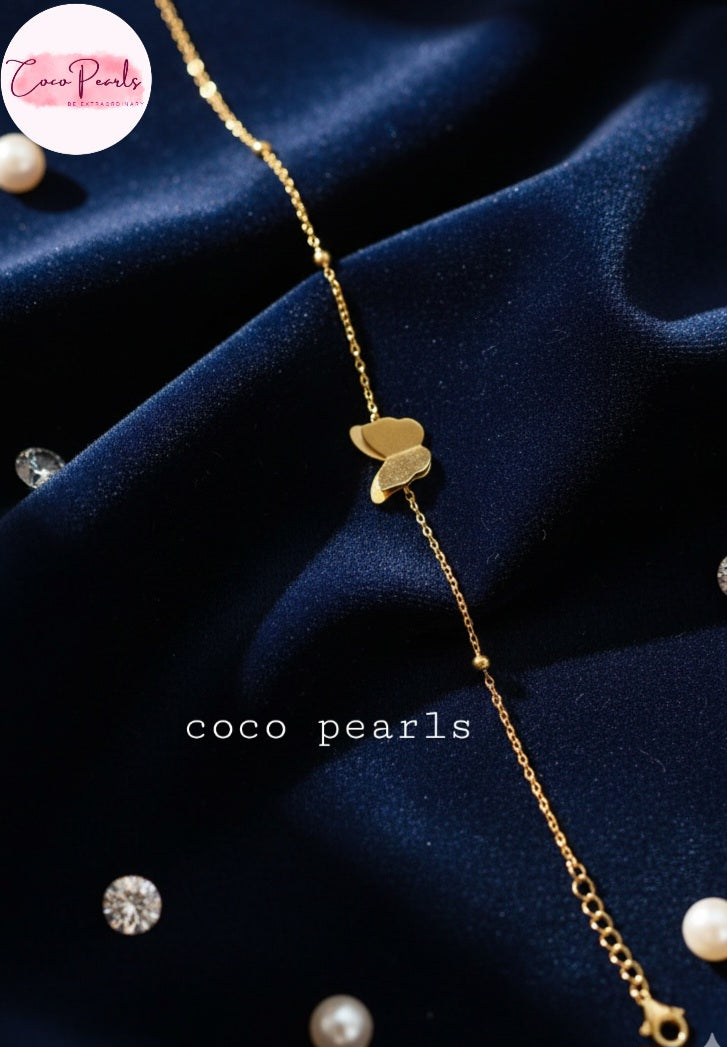 Coco Pearls Stainless Steel Anti Tarnish Gold butterfly whisper bracelet with heart charm on a dark blue fabric background