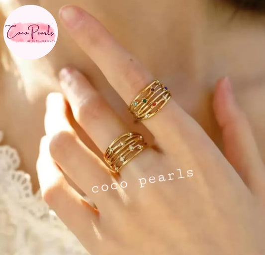Coco pearls stainless Steel anti tarnish close-up of a hand wearing two gold-toned multi-band rings with small colorful gemstone accents, against a warm skin-toned background