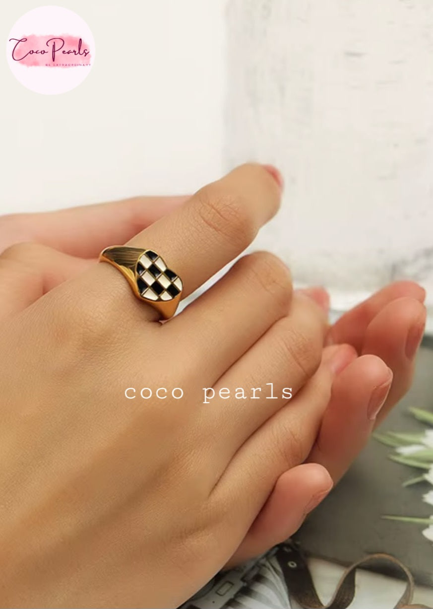 Coco pearls stainless Steel anti tarnish close-up of a hand wearing a gold signet-style ring with a black-and-white checkered face.