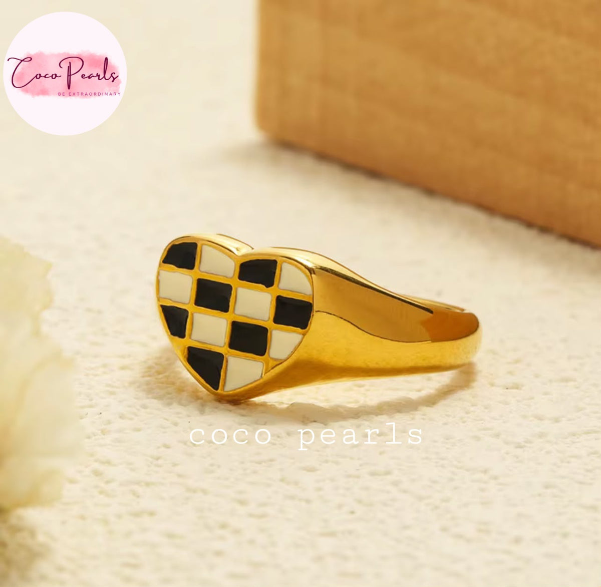 Coco pearls stainless Steel anti tarnish gold signet ring with a heart-shaped face featuring a black and white checkerboard pattern, displayed on a textured cream surface