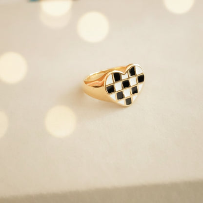 Coco pearls stainless Steel anti tarnish gold ring with a heart-shaped face featuring a black and white checkered pattern, photographed on a light gray surface. 