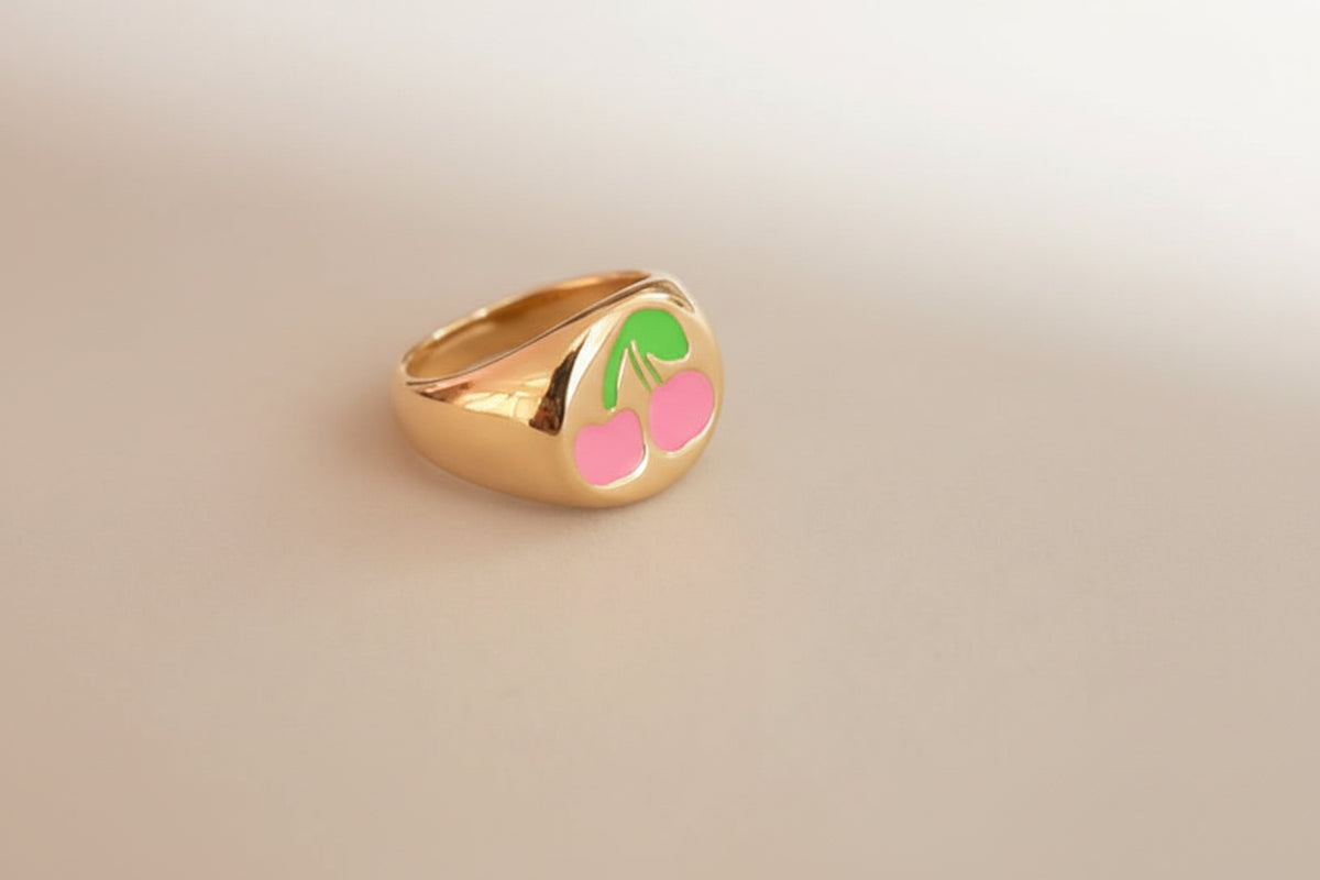 Coco pearls stainless Steel anti tarnish gold signet ring featuring a cherry design with a bright pink enamel body and a green stem, displayed on a neutral gray surface