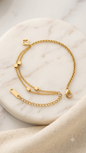 A delicate gold chain anklet with a small clover charm and box beads