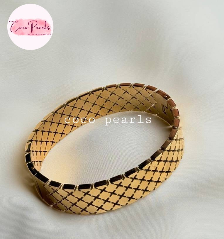Coco pearls stainless Steel anti tarnish gold-plated woven mesh bangle bracelet with black inlay details, displayed on a soft white fabric background.