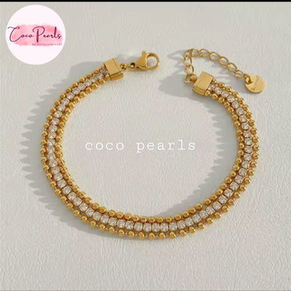 Coco pearls stainless Steel anti tarnish gold-plated tennis-style bracelet with rows of clear rhinestones, shown on a light textured background.