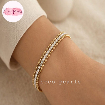 Coco stainless Steel anti tarnish close-up of a person's wrist wearing two delicate gold bracelets, each set with clear round stones.