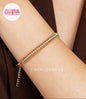 Coco pearls stainless Steel anti tarnish gold chain bracelet with a row of clear crystals, shown worn on a person's wrist against a dark brown background.