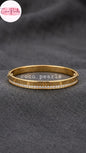Coco pearls stainless Steel anti tarnish gold-plated bangle bracelet with a row of clear faux-pearls and engraved lettering, displayed on a dark gray textured fabric background.