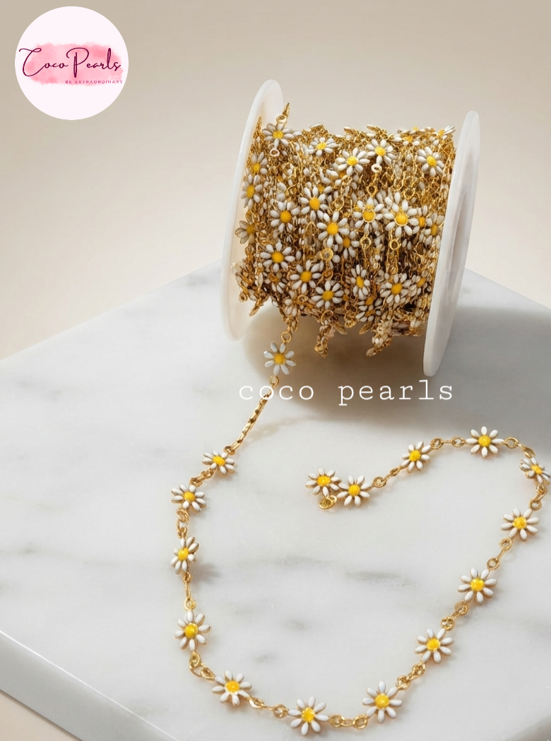 Coco pearls stainless Steel anti tarnish Gold chain daisy necklace with white enamel petals and yellow centers, shown draped from a spool on a light marble surface. 