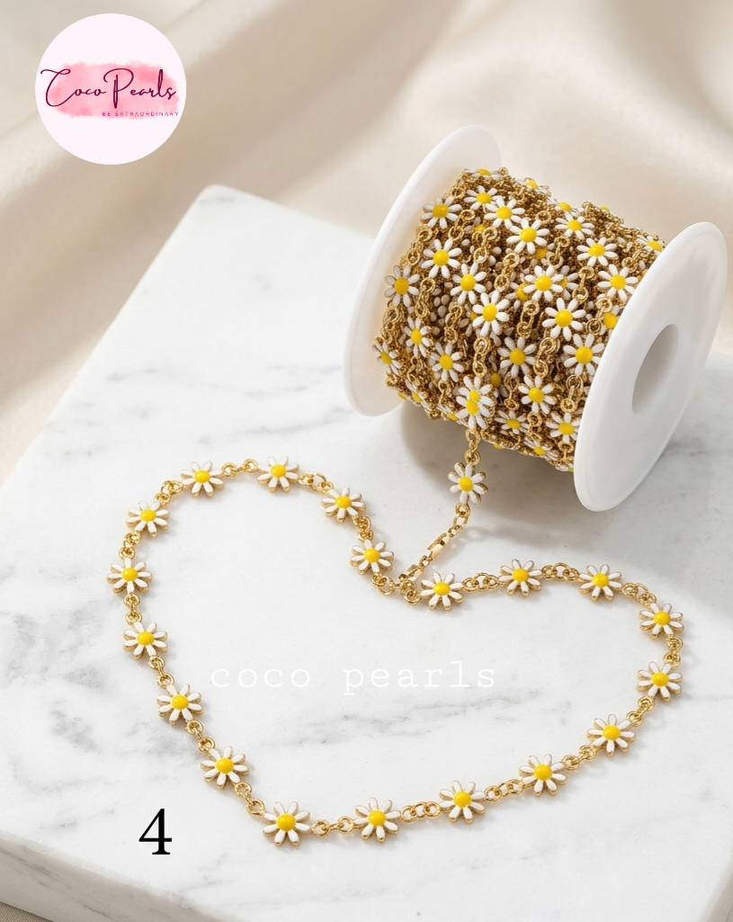 Coco pearls stainless Steel anti tarnish Gold chain embellished with small white daisy flowers, shown unspooled from a white spool on a white marble surface.