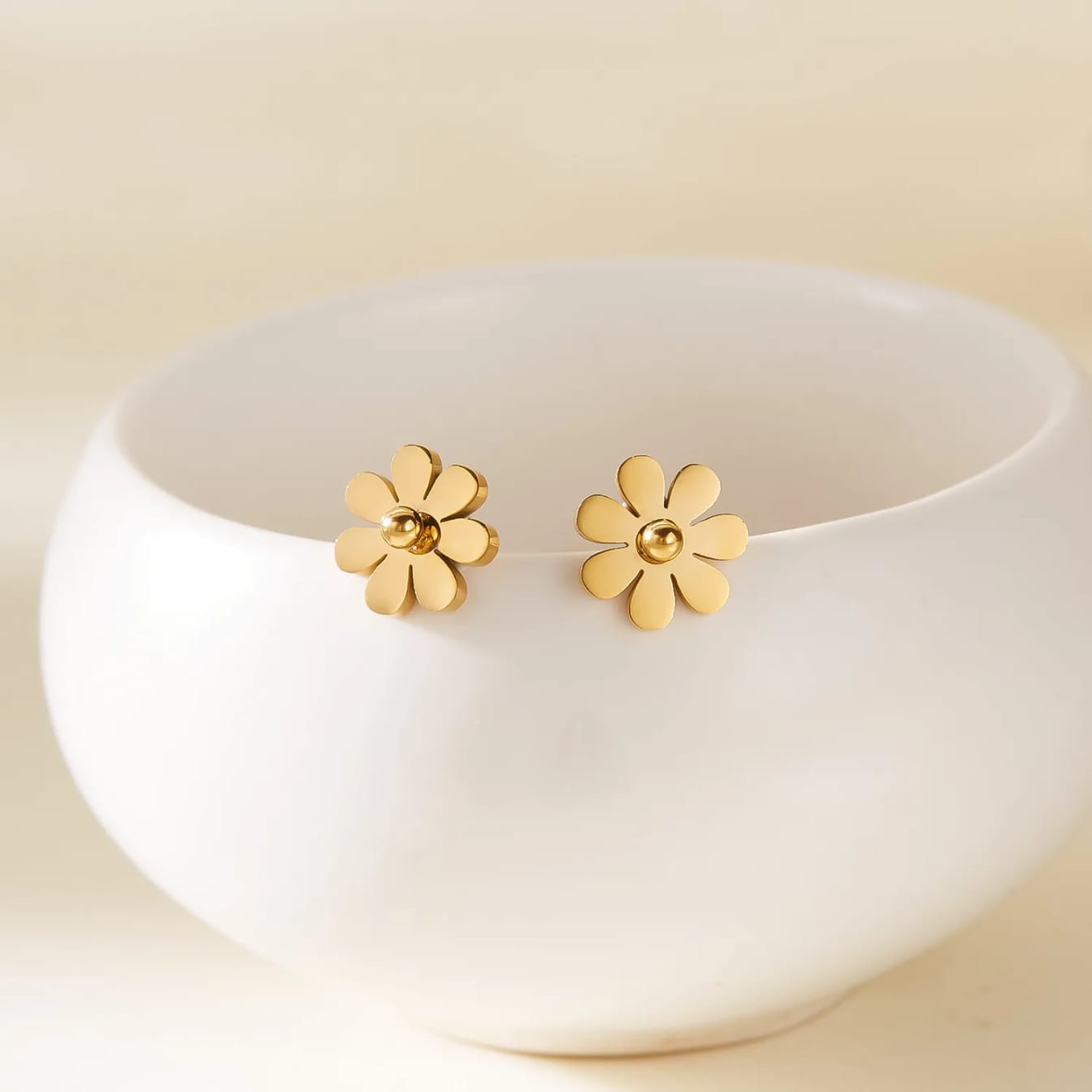 Coco pearls stainless Steel anti tarnish Gold flower-shaped earrings on a white dish with a beige background