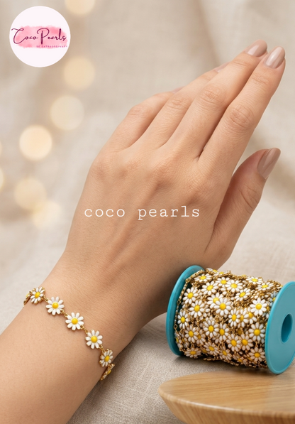 Coco pearls stainless Steel anti tarnish  close-up of a hand wearing a delicate bracelet made of small white daisy flowers with yellow centers and gold-toned metal. 