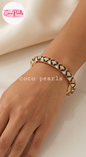 Coco pearls close-up of a person's hand and wrist wearing a gold bangle bracelet with black and white pearl-like geometric detailing. 