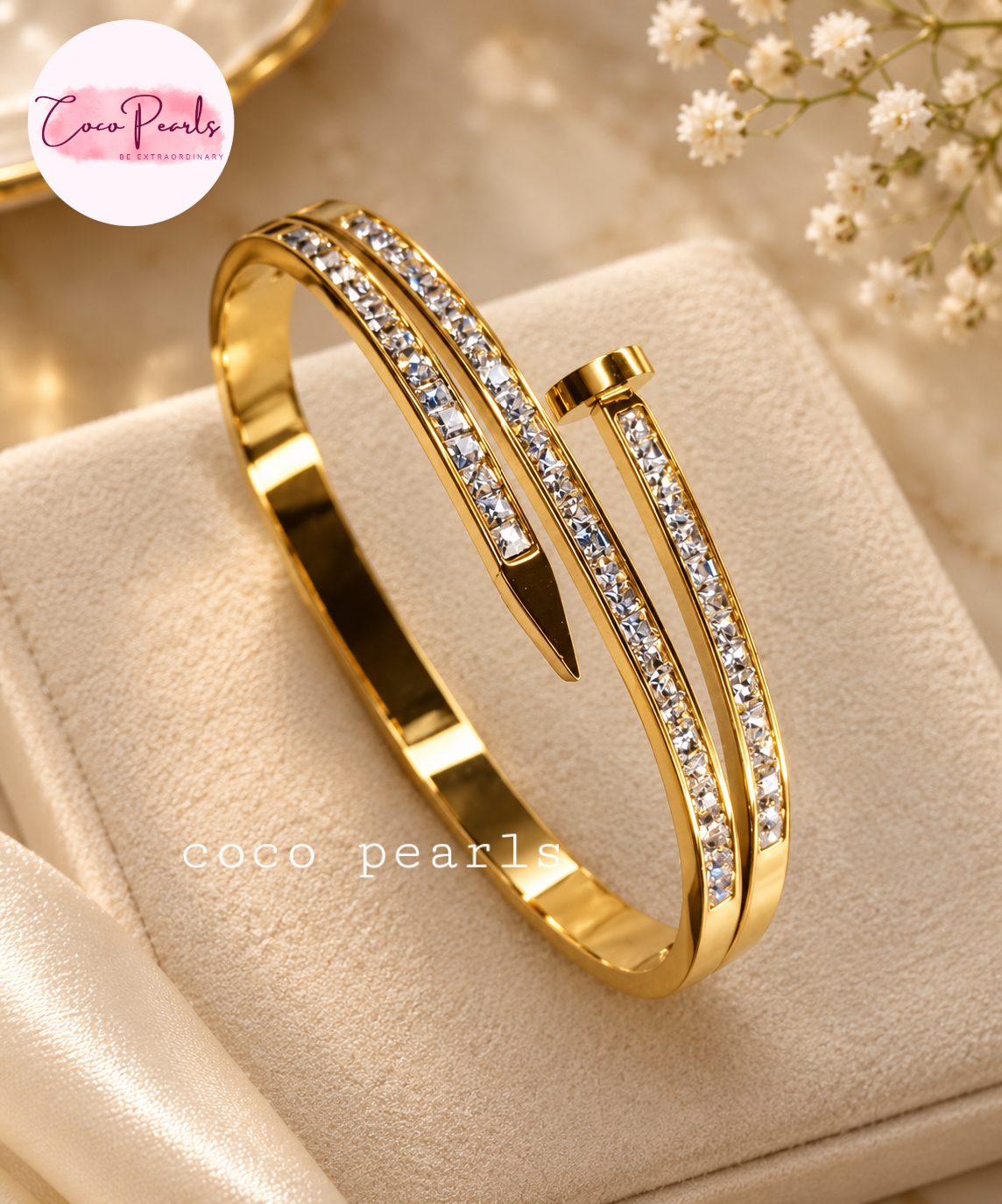 Coco pearls stainless Steel anti tarnish Gold-plated open cuff bangle bracelet with clear pavé crystal accents, displayed on a cream-colored jewelry cushion