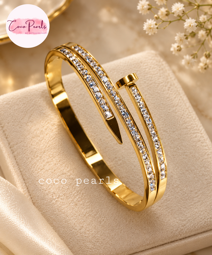 Coco pearls stainless Steel anti tarnish Gold-plated open cuff bangle bracelet with clear pavé crystal accents, displayed on a cream-colored jewelry cushion